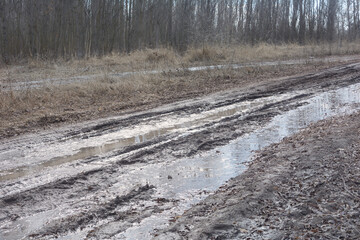 Dirt road with liquid mud and puddle in early spring. Traces from jammed car