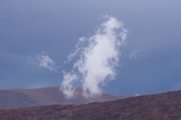 Poetic alpine landscape. Closeup view of a white cloud and mountain peak at sunset. 