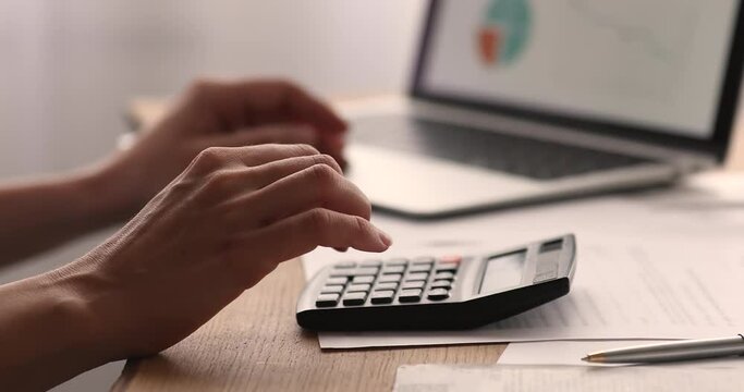 Close up young businesswoman summarizing costs of internet project, using calculator and computer accounting application data, planning budget or estimating taxes online, financial audit concept.