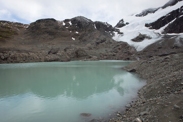 Alpine background. Glacier water lake high in the cordillera. View of the turquoise color water lake in the rocky mountaintop and Glacier Vinciguerra in the snowy peak. 