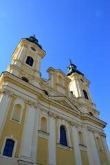 Baroque two-towered piarist church of St. Ladislav in Nitra, viewed from the street, spring clear blue skies. Jet trail and part of parking sign is visible in upper and lower right corner