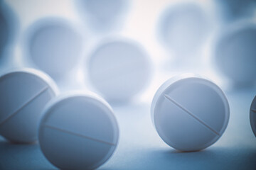A pile of white pills scattered on a white background with blue tinting. Selective focus.