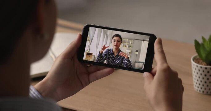 Close up young woman looking at cellphone screen, holding video call zoom negotiations meeting with indian colleague, discussing project or working issues remotely, distant communication concept.