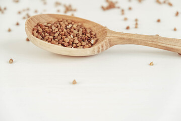 Buckwheat in a wooden spoon on a white background. Copy, empty space for text
