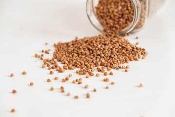 Buckwheat in a glass jar scattered on a wooden white table. Copy, empty space for text