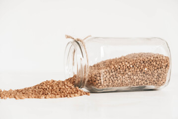 Buckwheat in a glass jar scattered on a wooden white table. Copy, empty space for text
