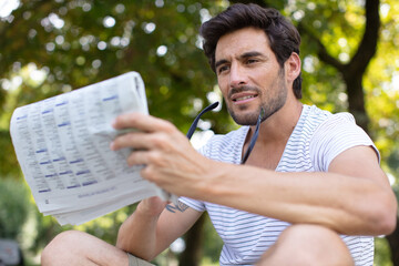 Fototapeta premium bearded young man reading newspaper on the bench