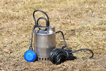 Well pump with a long black cable on the background of old grass. Pump with power cable and...