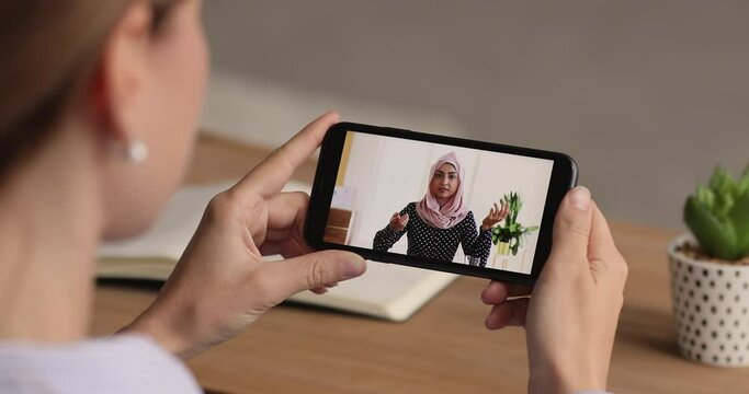Close up focus on cellphone screen with young indian woman in hijab holding negotiations video call meeting with female colleague, giving educational lecture or advice, distant zoom communication.