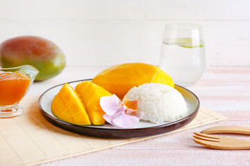 Plate with tasty rice and mango on light wooden background