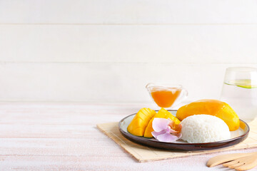 Plate with tasty rice and mango on light wooden background