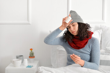 Sick young woman with pills and thermometer at home