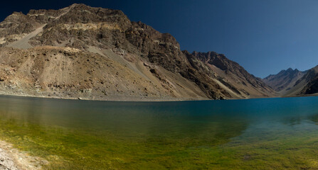 The colorful lake called Inca Lagoon in the Andes mountain range. The blue glacier water and yellow shallows surrounded by rocky mountains.