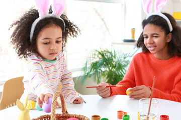 Little African-American girls painting Easter eggs at home