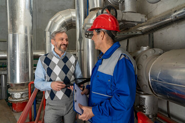 Smiling Manager and Worker in Red Hardhat and Blue Uniform Having Conversation in Industrial Interior