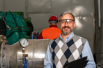 Smiling Manager With Digital Tablet Standing in Mechanical Room and Looking at Camera