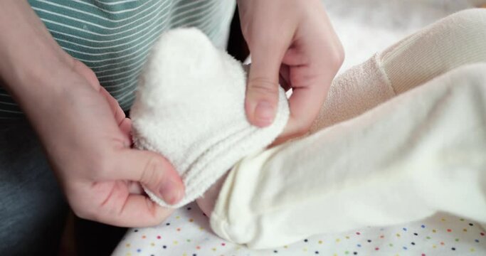 Mother putting socks on her newborn baby feet at home