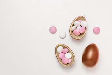 Minimalistic Easter background. Chocolate egg with white and pink candy-dragees on a white table. the concept of an Easter greeting card.