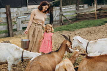 Happy mother and her daughter spend time on an eco farm among goats.