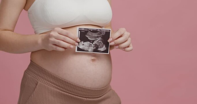 Memory of pregnancy. Unrecognizable pregnant woman holding sonography picture near her big belly