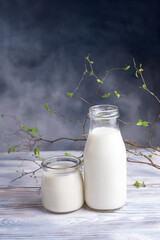 Bottle and jar of milk on a white wooden table with a beautiful branch