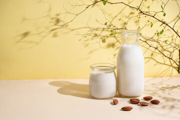 Jar and bottle with almond milk and almonds on a yellow background in sunlight, vegetarian milk.
