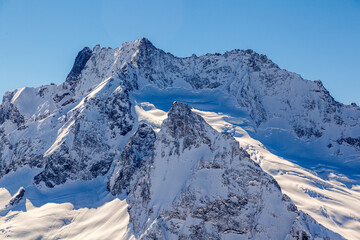 Caucasus Mountains, Panoramic view of the ski slope with the mountains Belalakaya, Sofrudzhu and Sulakhat on the horizon in winter day. Dombai ski resort, Western Caucasus, Karachai-Cherkess, Russia.