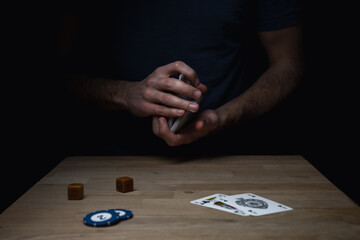 Man in blue shirt against dark background shuffling a deck of red cards at a wooden table. Games cards playing poker gambling.