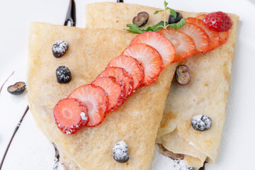 dessert of pancakes with strawberries, blueberries and chocolate topping on a plate
