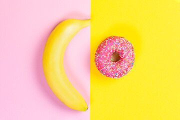 Banana and donut with pink icing on a yellow-pink background. Flat lay. The concept of choice and nutrition