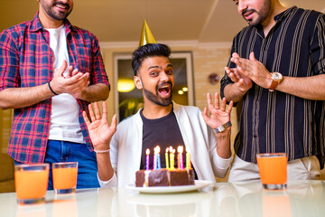 Excited arabian man ready to blow out candles on cake on birthday party with happy friends in the...