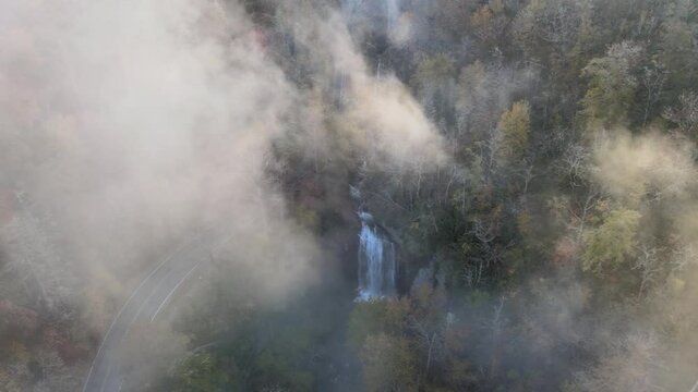Autumn colors in the fog of Looking Glass falls near Brevard. Aerial view with pan to sunshine  