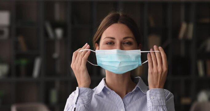 Caucasian happy 35s woman looking at camera, taking off protective disposable facemask, feeling relieved breathing fresh air indoors, personal safety quarantine covd19 measures, pandemic outbreak.