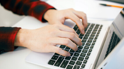 Fototapeta na wymiar Close up of a mans hands on the keyboard of a laptop . Young man working from home. High quality photo
