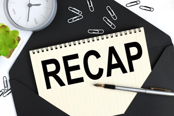 Recap. text on a sheet of notepad on a black envelope on a light background