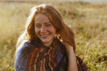 Naklejka premium On the meadow grass sits a beautiful girl without makeup with freckles on her face smiling broadly with a white-toothed smile. High quality photo