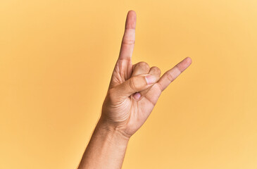 Arm and hand of caucasian man over yellow isolated background gesturing rock and roll symbol, showing obscene horns gesture