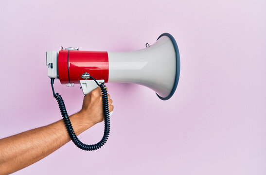 Hand of hispanic man holding megaphone over isolated pink background.