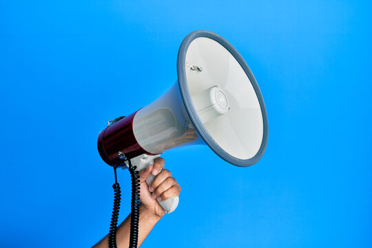 Hand of hispanic man holding megaphone over isolated blue background.