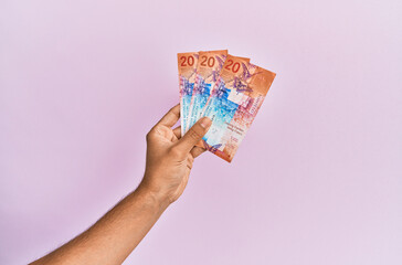 Hispanic hand holding 20 swiss franc banknotes over isolated pink background.