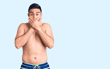 Young handsome man wearing swimwear shocked covering mouth with hands for mistake. secret concept.