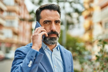 Middle age businessman with serious expresison talking on the smartphone at the city.