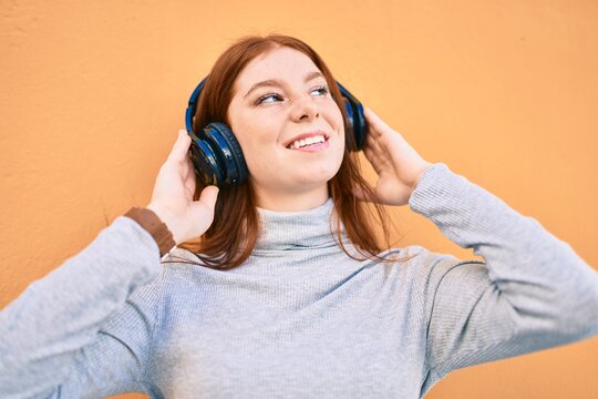 Young irish teenager girl smiling happy listening music using headphones at the city.