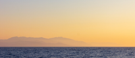 Seascape with fog and mountains. Seascape at sunset. View from the sea to the mountains in the haze. Dramatic scenes and the beauty of nature. Copy space