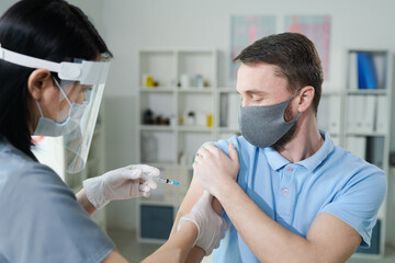 Young man holding sleeve of his shirt while female clinician vaccinating him