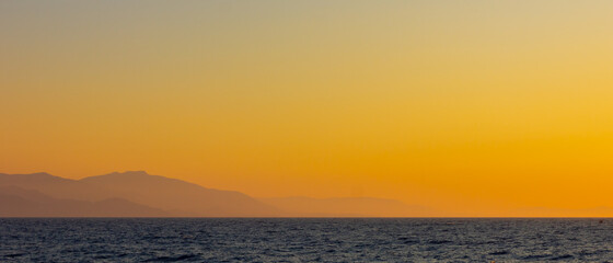 Obraz premium Seascape with fog and mountains. Seascape at sunset. View from the sea to the mountains in the haze. Dramatic scenes and the beauty of nature. Copy space