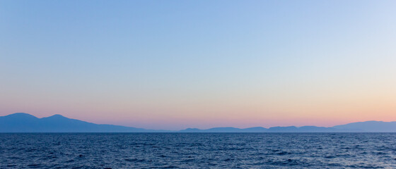 Obraz premium Seascape with fog and mountains. Seascape at sunset. View from the sea to the mountains in the haze. Dramatic scenes and the beauty of nature. Copy space