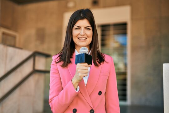 Middle age reporter woman holding microphone doing television speech outdoors