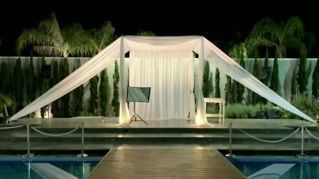 Jewish traditions wedding outdoor ceremony. Wedding canopy (chuppah, hupa) made of white fabric against the background of evening sky, palms and an artificial reservoir decorated with balloons. HD