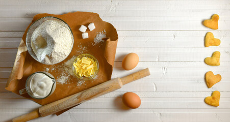 Ingredients for baking heart cookies. Flour the butter cream on a brown paper substrate. A rock and eggs on a wooden white background.